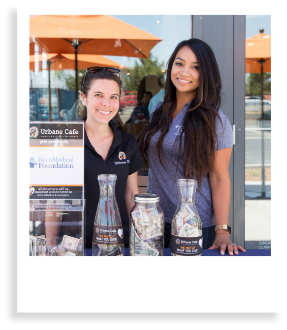 two women standing in front of urbane cafe smiling with jars full of raised money