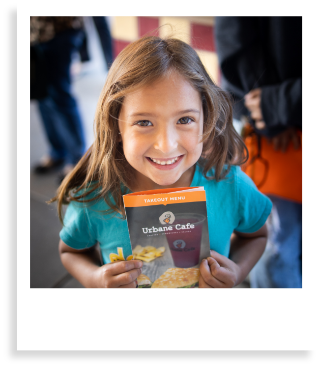 little girl smiling holding urbane cafe brochure