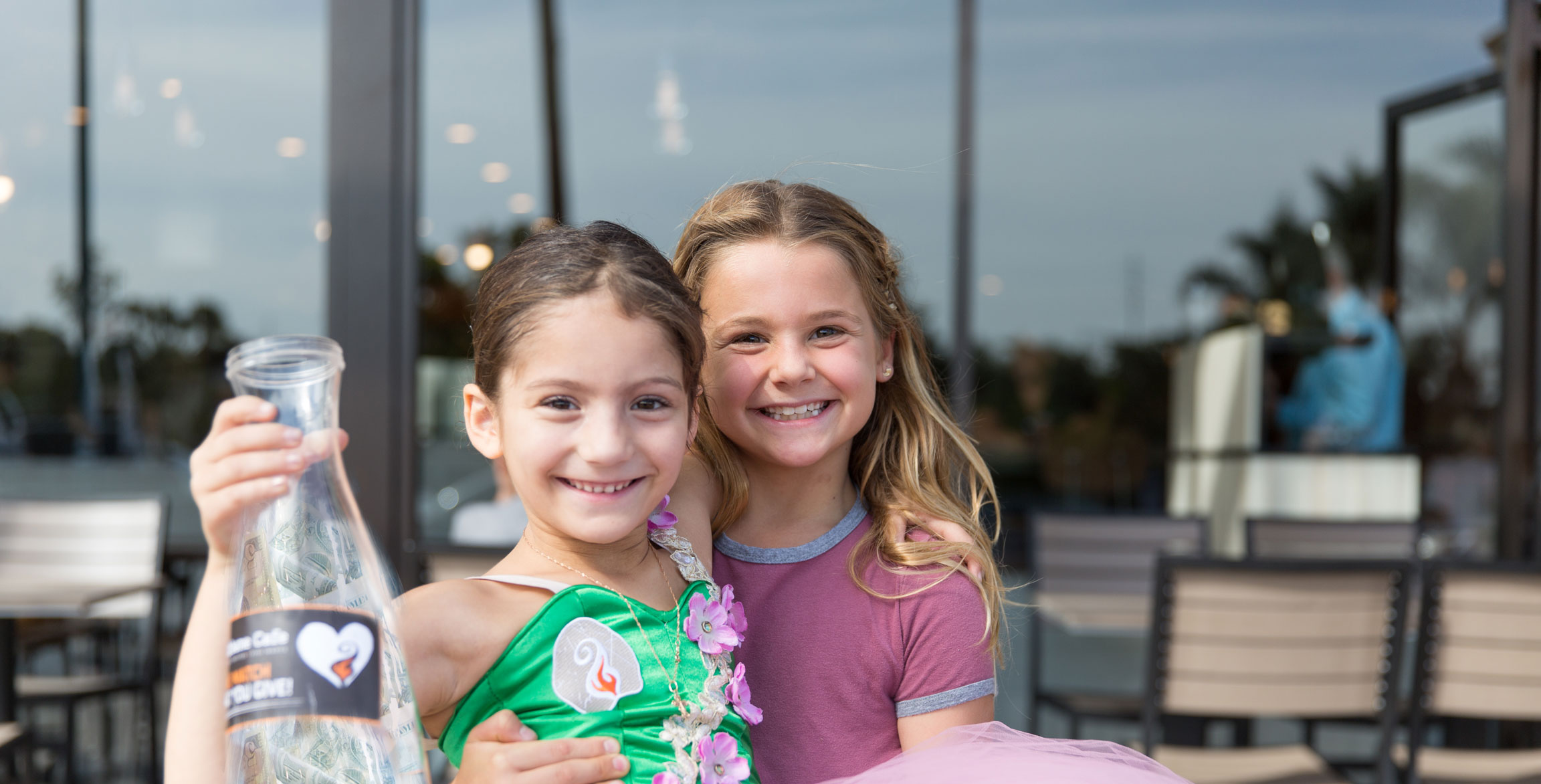 two little girls smiling holding fundraising jar in front of urbane cafe